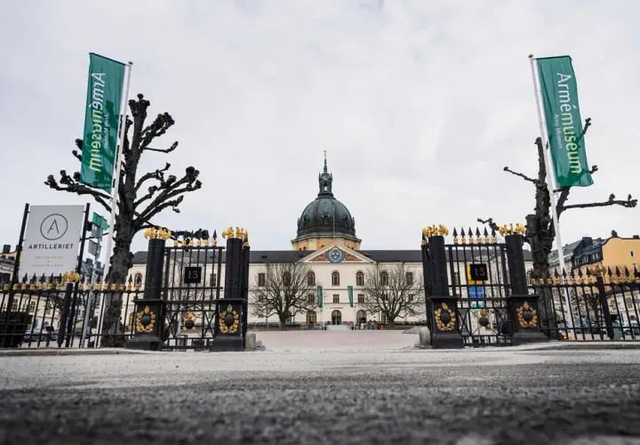 Grön flagga med texten "Armémuseum" vid krigsmuseum Stockholm. Imponerande byggnad med kupol och staket.