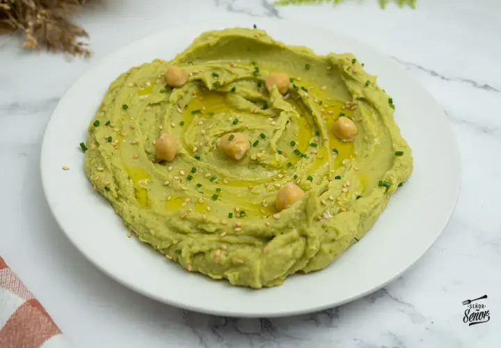 Hummus de aguacate cremoso, decorado con garbanzos, aceite de oliva, semillas de sésamo y cebollino. ¡Un entrante delicioso!