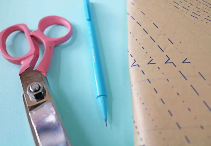 Pink scissors and a blue pen lie next to a piece of pattern paper, ready for a project to place on fold.
