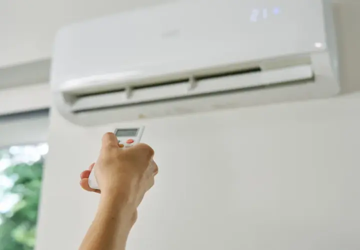 Dłoń trzymająca pilot do klimatyzacji, która chłodzi pomieszczenie. Zastanawiasz się, czy klimatyzacja pobiera dużo prądu?