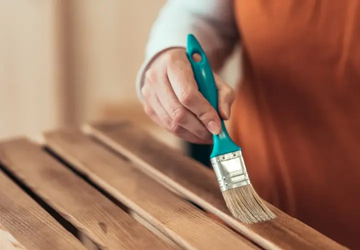 Mano con brocha lijando listones de madera barnizada para restaurar un mueble.