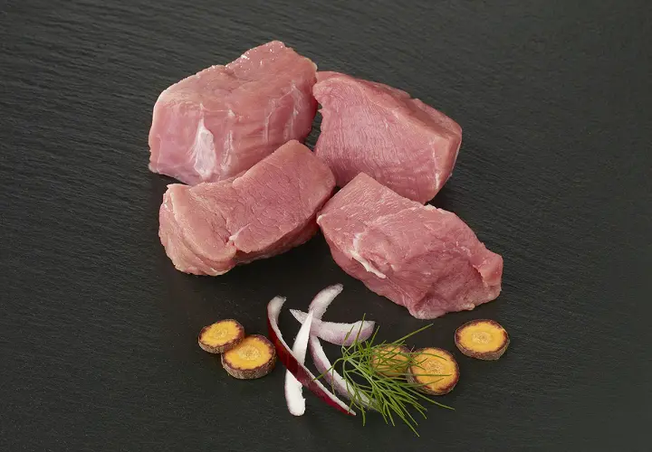 Quatre morceaux d'épaule de veau crus, accompagnés de rondelles de carottes, d'oignon rouge et d'aneth sur fond noir.