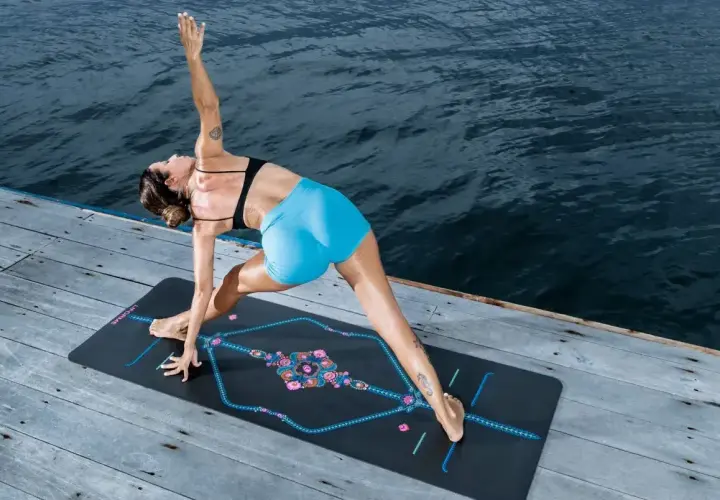 Kobieta w pozie jogi na macie nad wodą, ćwicząca asanę. Stanowi to idealne tło do praktyki yoga nidra.