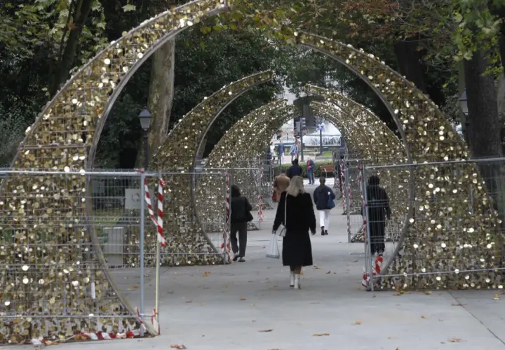Personas pasean bajo arcos dorados decorados con luces, preparándose para el encendido de luces en Oviedo.