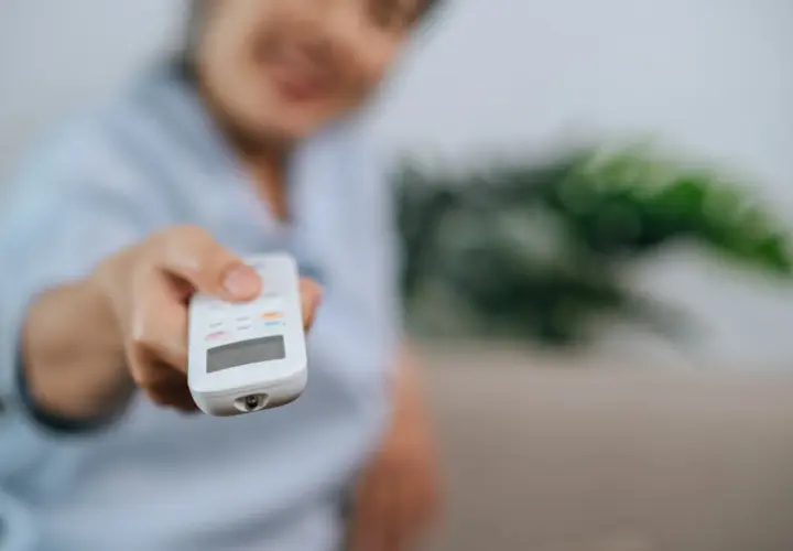 Persona sonriente ajusta el aire acondicionado con el mando. Controla la potencia aire acondicionado kw para un confort ideal.