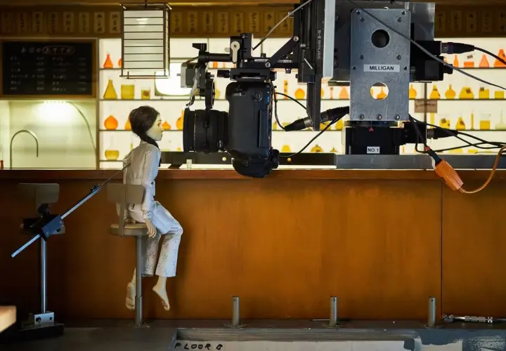 Bambola seduta su uno sgabello, pronta per essere animata in stop motion. La telecamera è posizionata sopra di lei, pronta a catturare ogni movimento.