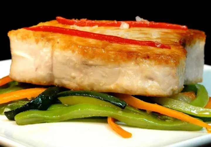 Bonito jugoso sobre verduras salteadas, con tiras de pimiento rojo.
