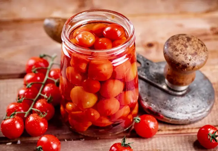 Glas voller Tomaten, bereit zum Einkochen wie Oma. Frische Kirschtomaten und ein Einkochgerät auf Holzuntergrund.