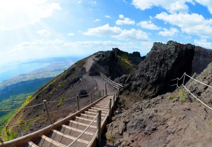 Sentiero sul cratere del Vesuvio, un vulcano attivo. Scale di legno e corde guidano i visitatori verso la cima, con vista sul golfo.