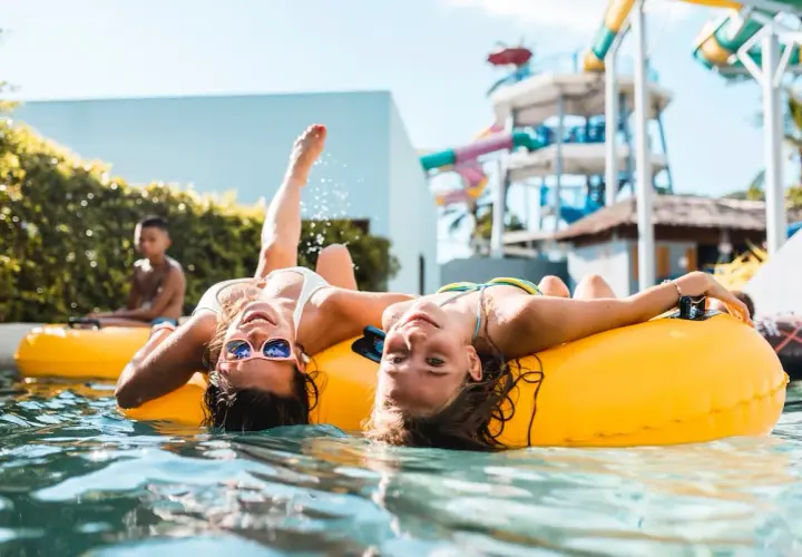 Dwie dziewczyny relaksują się na dmuchanych kołach w basenie. W tle widać zjeżdżalnie wodne, sugerujące, że to największy aquapark w Europie.