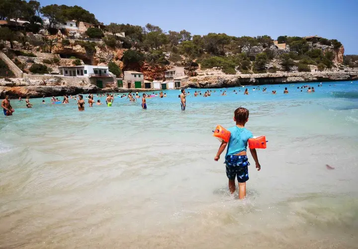 Sonnige Bucht mit vielen Menschen, ein kleiner Junge mit Schwimmflügeln geht ins Meer. Perfekte urlaubsziele mit kindern.