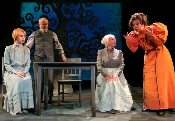 Scena z Teatru Groteska. Cztery postacie w strojach z epoki, w tym młoda dziewczyna, starszy mężczyzna i dwie kobiety, rozmawiają przy stole.