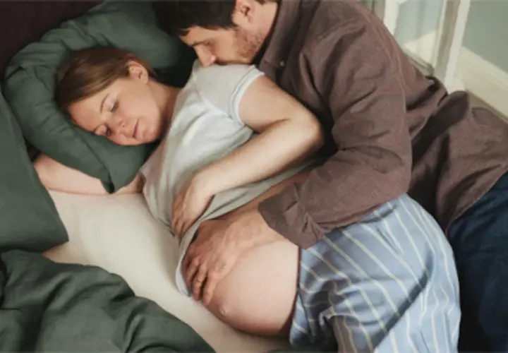 En man kramar en gravid kvinna som sover. Hans hand vilar på hennes mage, ett tecken på lyckad hinnsvepning och förväntan inför barnets ankomst.
