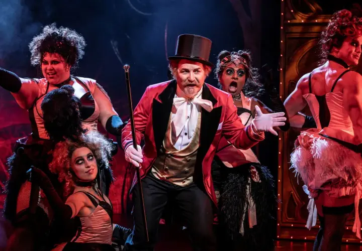 Scen från Moulin Rouge! The Musical i Stockholm. En cirkusdirektör med cylinderhatt och röd kavaj leder en färgstark ensemble.
