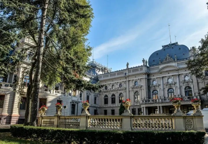 Majestatyczny pałac poznański z ozdobną balustradą i kwitnącymi kwiatami, otoczony zielenią.