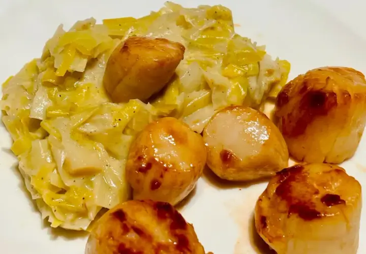 Saint-Jacques poêlées sur un lit de fondue de poireaux crémeuse, un plat savoureux et réconfortant.