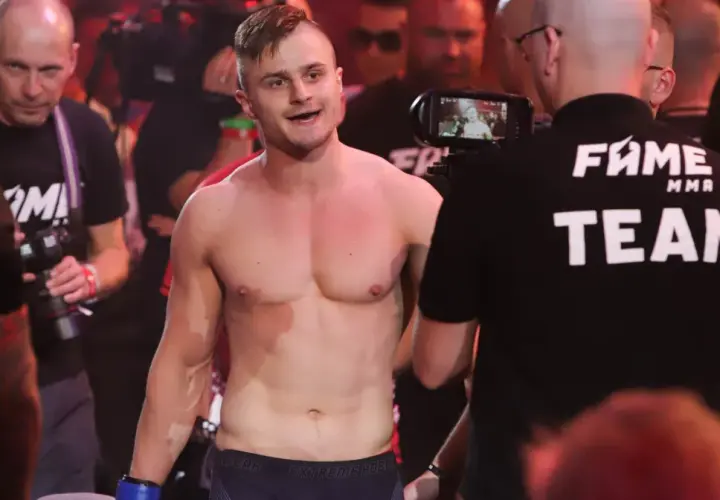 Amadeusz Ferrari, zawodnik MMA, wychodzi na ring, otoczony przez ekipę i kamery.