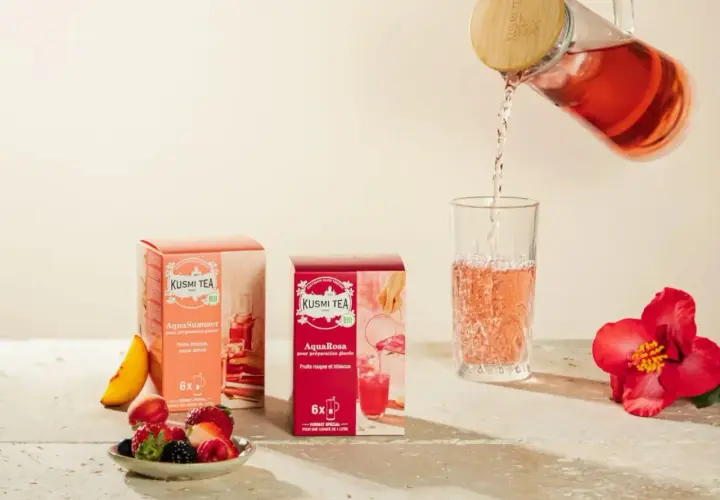 Kusmi Tea AquaRosa i AquaSummer w pudełkach, nalewanie różowej herbaty do szklanki. Obok owoce i hibiskus.