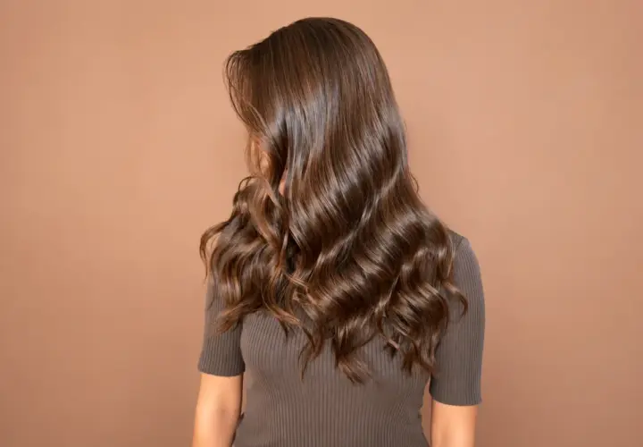 Melena larga y ondulada de color avellana pelo, con reflejos brillantes sobre fondo marrón.