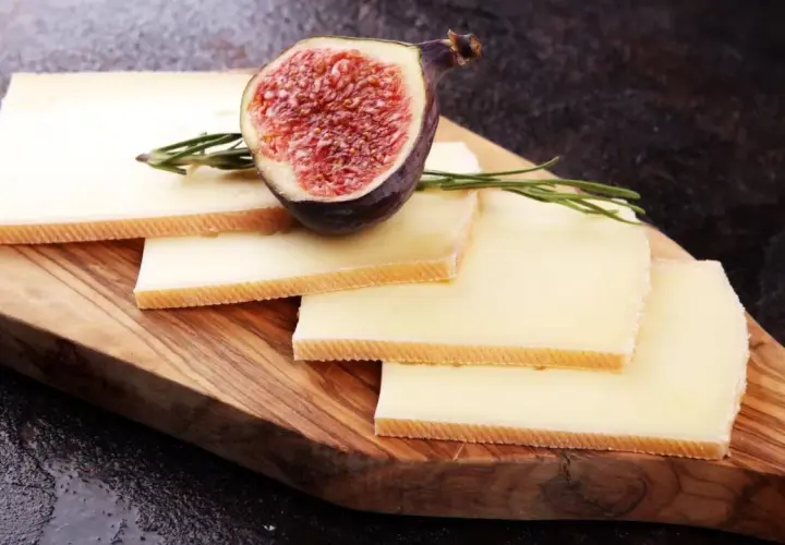 Tranches de fromage à raclette sur planche en bois, garnies d'une figue coupée et de romarin. Parfait pour une recette raclette 6 personnes.