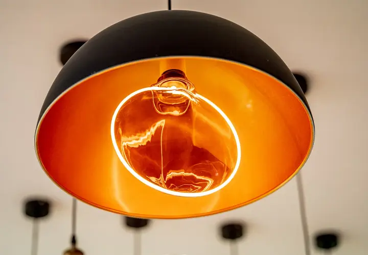 Lámpara colgante moderna con interior dorado y una bombilla decorativa Edison encendida, creando un ambiente cálido.