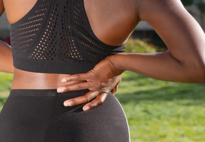Une femme en tenue de sport ressent une douleur barre dans le dos, sa main posée sur la zone sensible.