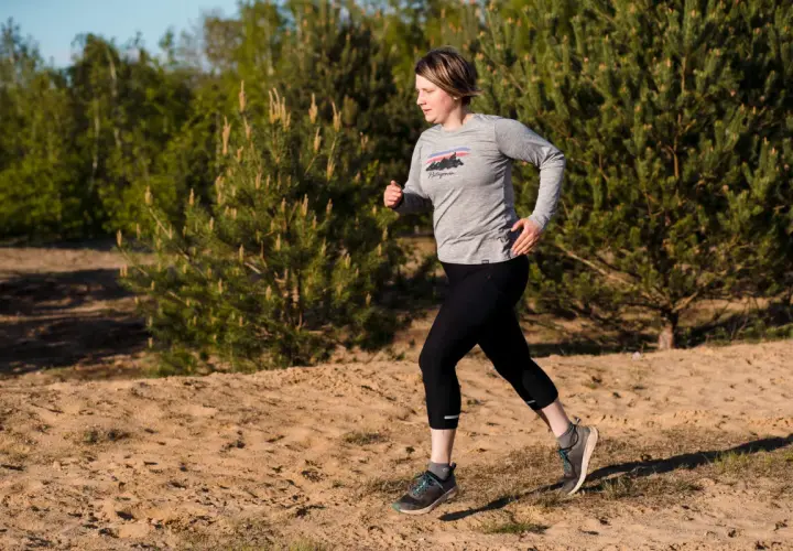 Frau beim **trail running** auf sandigem Untergrund, umgeben von Kiefern und Bäumen.