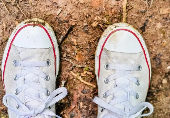 Białe trampki z czerwonymi akcentami, lekko zabrudzone ziemią, czekają na czyszczenie.