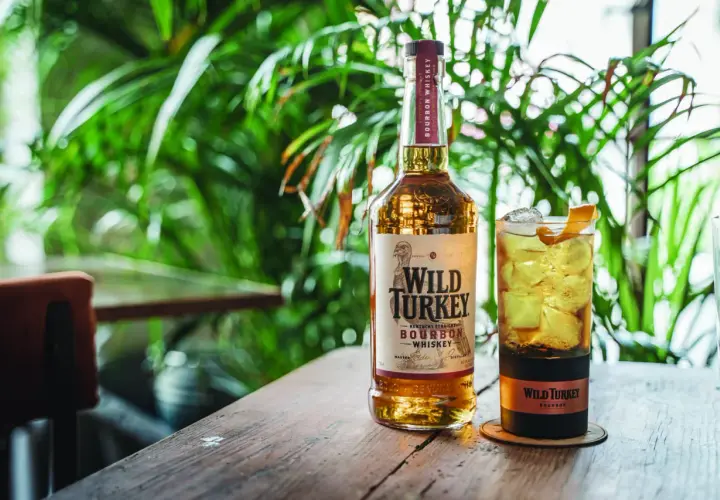 Un bicchiere di cocktail con bourbon Wild Turkey, ghiaccio e scorza d'arancia, accanto alla bottiglia.