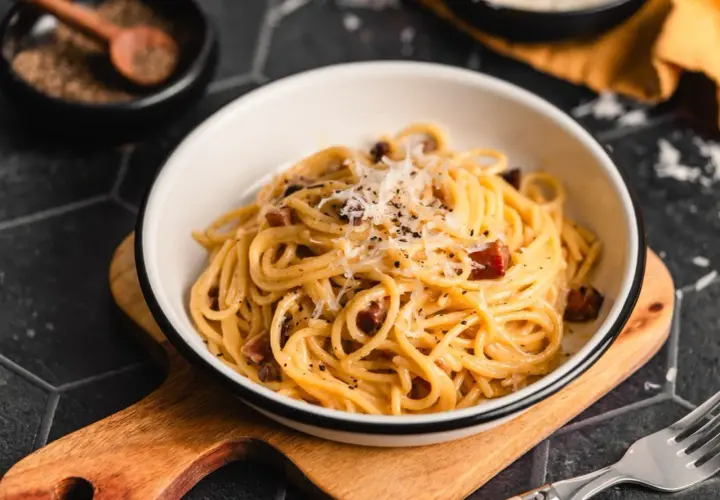 Ein Teller Spaghetti mit cremiger Sauce, garniert mit geriebenem Parmesan und schwarzen Pfefferkörnern. Darin versteckt sich leckerer Schinken für die perfekte Schinken Carbonara.