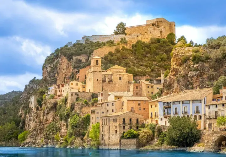Pueblo de cambrils de muntanya aferrat a un penya-segat rocós, amb cases de colors i un castell imponent al cim.
