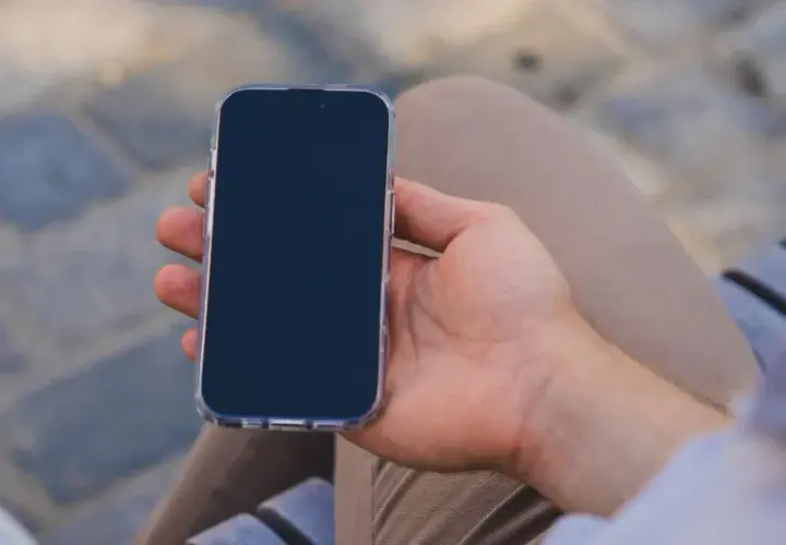 Mężczyzna trzyma iPhone'a w przezroczystym etui. Zastanawia się, jak wyłączyć iPhone'a, aby oszczędzić baterię.