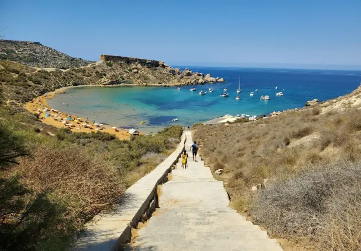 Malta, kwiecień: słoneczna pogoda zachęca do spaceru schodami w dół do zatoki z turkusową wodą i łodziami.