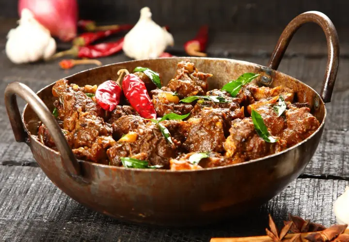 Aromatyczny gulasz z jagnięciny w miedzianym naczyniu, ozdobiony papryczkami chili i liśćmi curry.