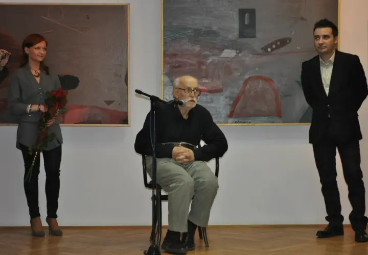 Konrad Wieniawa-Narkiewicz siedzi przy mikrofonie, obok niego stoi kobieta z kwiatami i mężczyzna w garniturze.