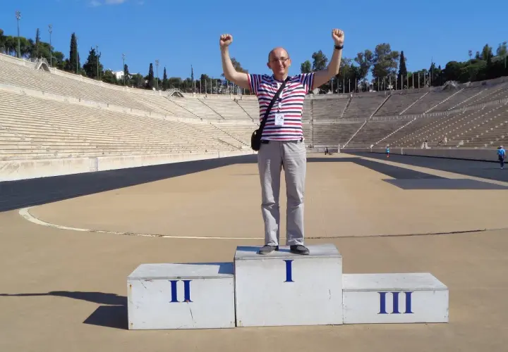 Mężczyzna z podniesionymi rękami na podium w historycznym stadionie panatenajskim.