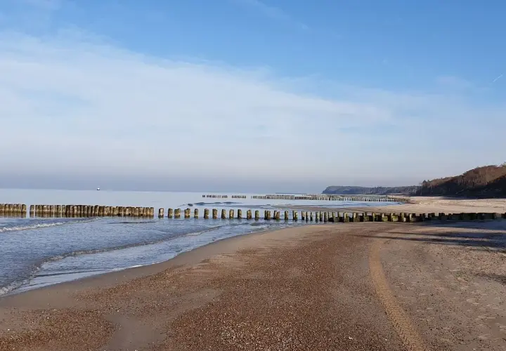 Spokojna plaża w Rusinowie z drewnianymi falochronami. Idealne miejsce na relaks i podziwianie widoków.