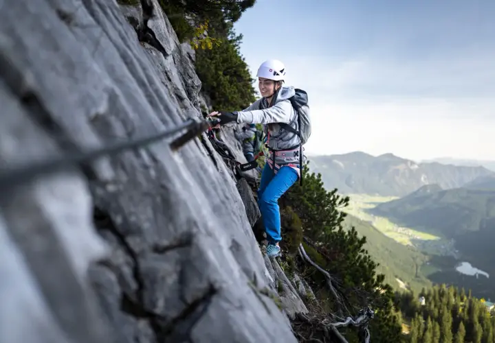 Uśmiechnięta kobieta na via ferrata dla początkujących, z widokiem na dolinę.