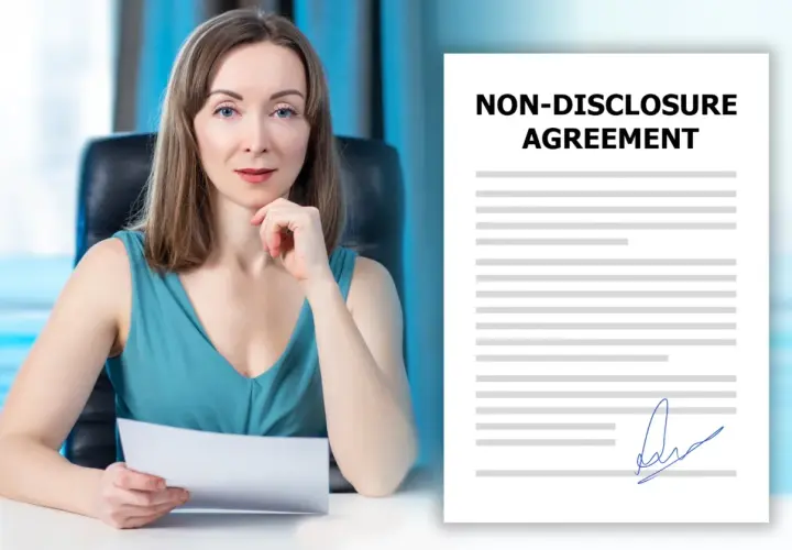 Kobieta w biurze trzyma dokument. Obok widoczny jest podpisany dokument "Non-Disclosure Agreement", czyli umowa o zachowanie poufności.