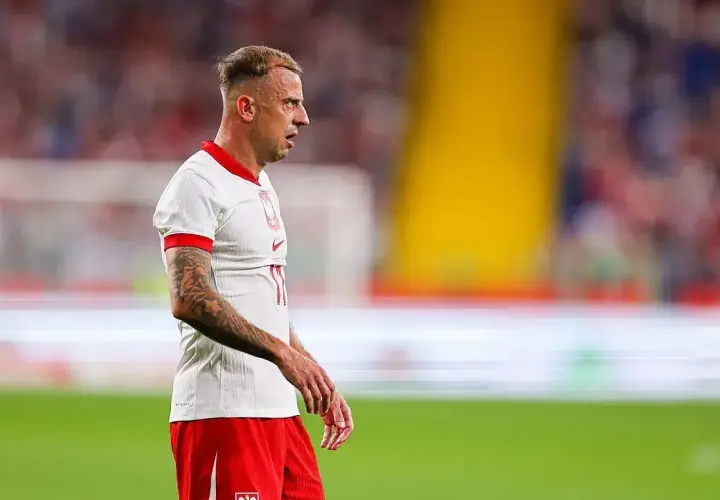 Piłkarz Kamil Grosicki w białej koszulce i czerwonych spodenkach, z tatuażami na ramieniu. Jego majątek to wynik ciężkiej pracy na boisku.