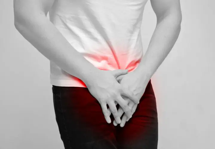 Mężczyzna trzyma ręce na podbrzuszu, gdzie widoczne są czerwone plamy bólu. Może to symbolizować dyskomfort związany z masowaniem prostaty.