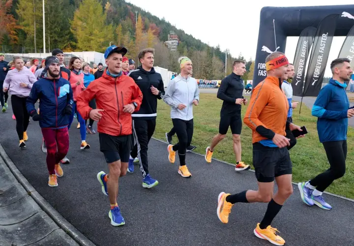 Grupa biegaczy w kolorowych strojach, jak z filmu o bieganiu, startuje na trasę. W tle las i bramka mety Puma.