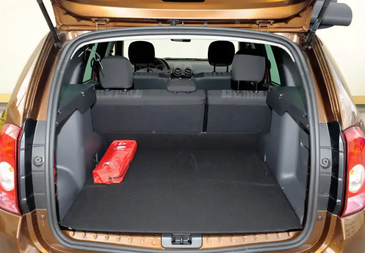 Otwarty bagażnik Dacia Duster, pokazujący jego pojemność. Czerwona apteczka leży na czarnym dywaniku.