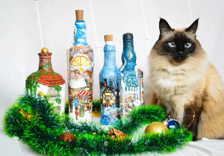 Urocze butelki ozdobione techniką decoupage na szkle, z zimowymi scenkami. Obok siedzi piękny kot.