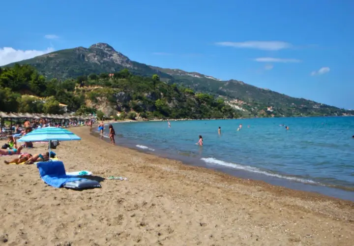 Słoneczna plaża na Zakynthos w czerwcu. Ludzie kąpią się w turkusowym morzu, opalają pod parasolami. Idealna pogoda na wakacje.