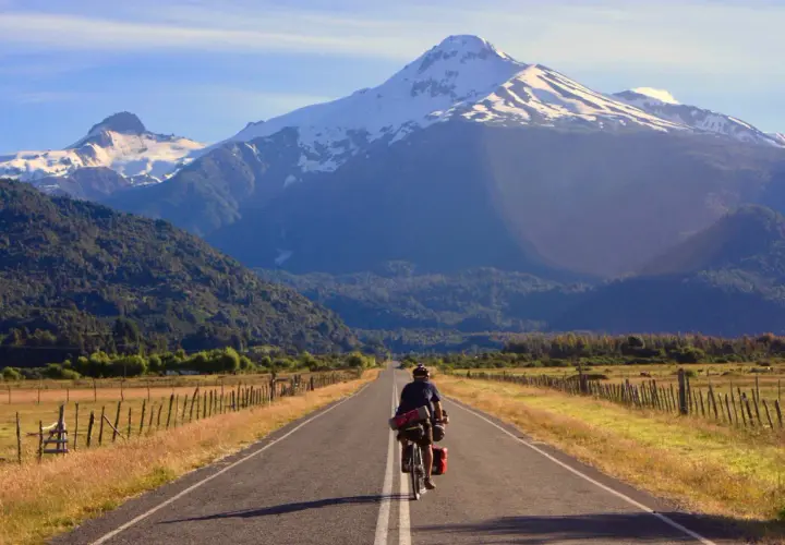 Ciclista pedaleando por la Carretera Austral, con imponentes montañas nevadas de fondo.