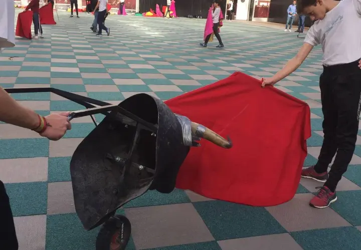 Jóvenes aprenden a torear con un capote y un toro de utilería.