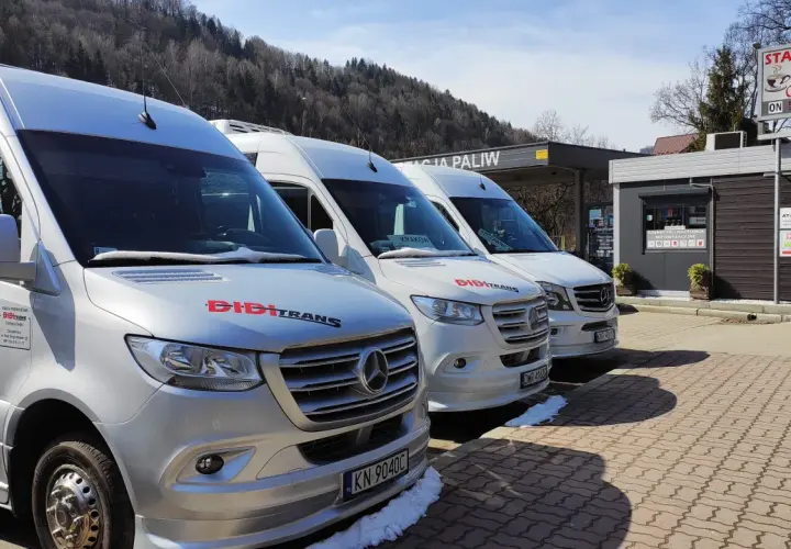 Trzy białe busy marki Mercedes stojące pod zadaszeniem stacji paliw.
