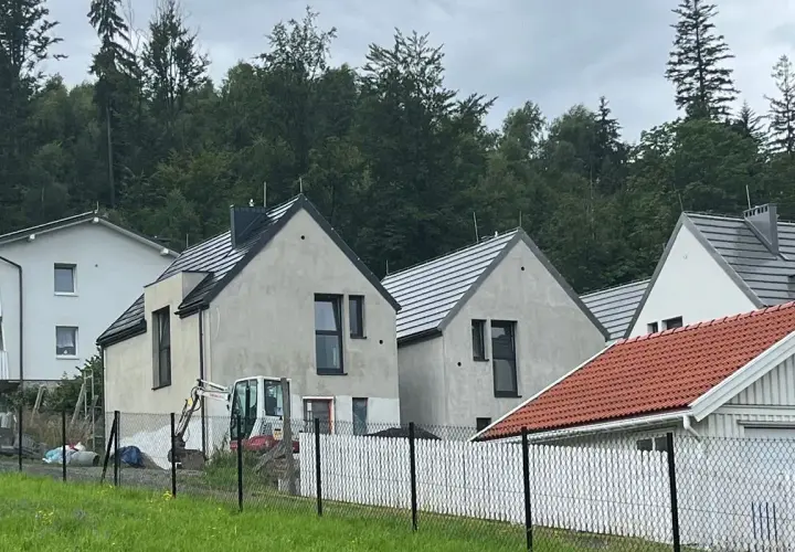 Nowe domy w stylu skandic hus, w budowie, z koparką na placu. W tle las.