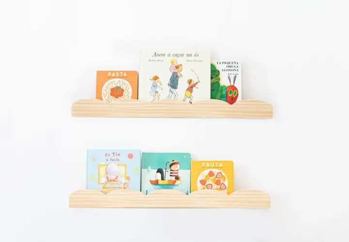 Dos estantes nube de madera con libros infantiles. En el superior: "Pasta", "Anem a caçar un ós" y "La pequeña oruga glotona". En el inferior: "En Tin a taula", un libro de pingüinos y "Fruta".